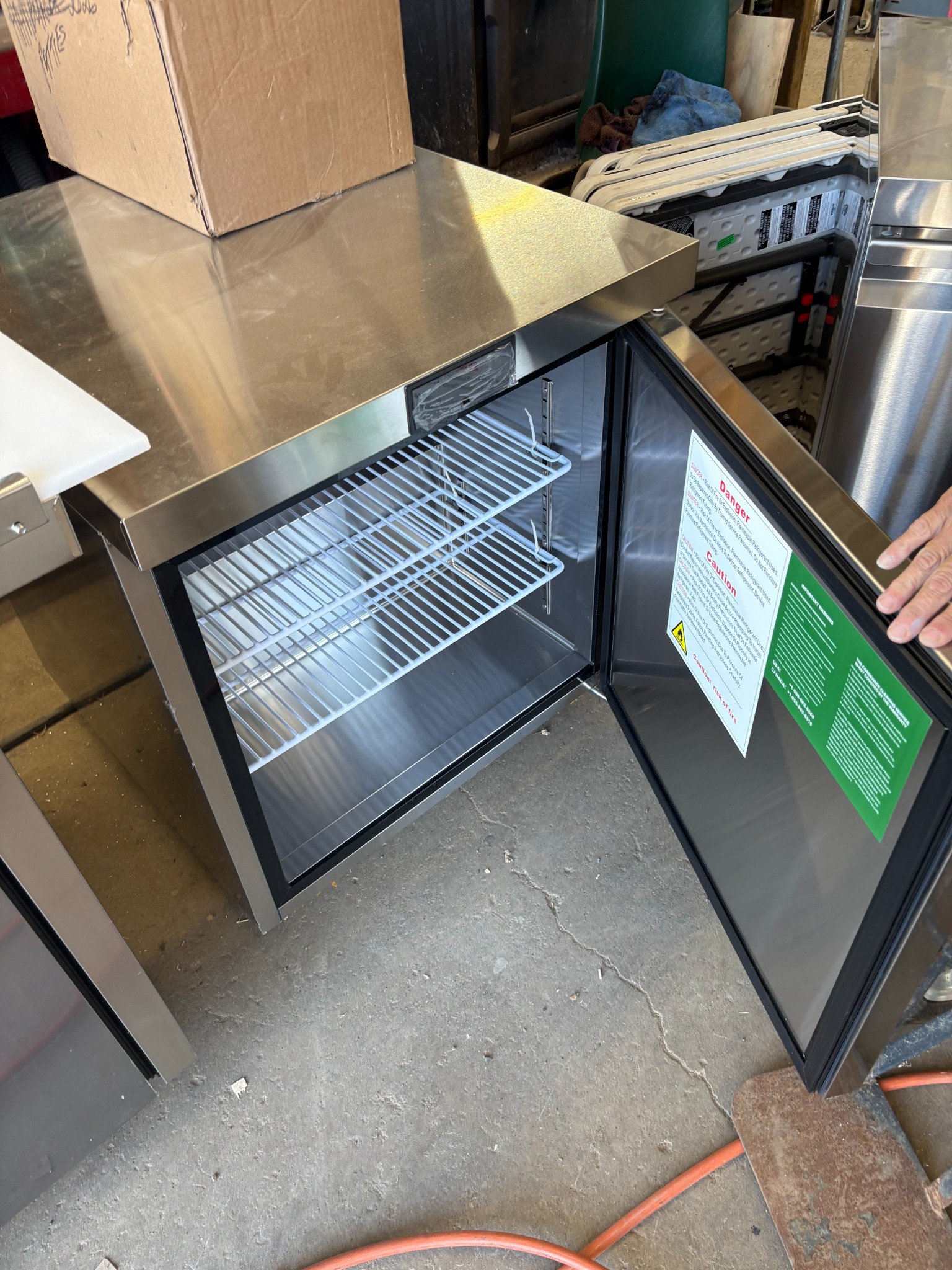 Open stainless refrigerator in the workshop, not yet installed